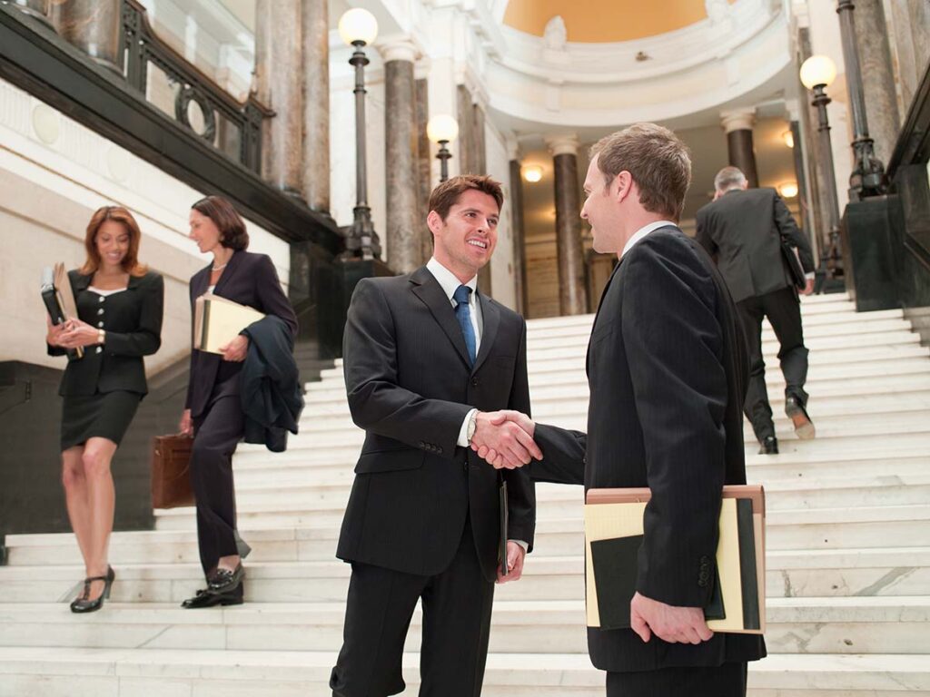 Legal professionals shaking hands on stairs of courtroom.