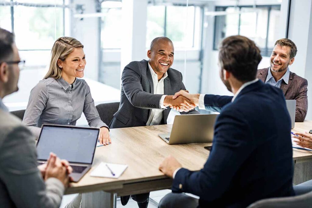 Group of business professionals in meeting shaking hands and smiling.